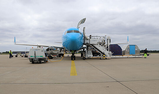 Ein blaues Luftfahrzeug mit elektrisch betriebenen Abfertigungsgerät, es werden 2 Frachtcontainer verladen. 